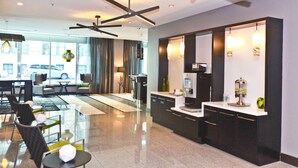 Un hall d’hôtel moderne avec une cloison en verre, un espace salon et une kitchenette.
