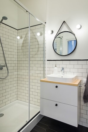 A modern bathroom with a glass-enclosed shower, a white sink with a wooden countertop, and a mirror with a black frame.