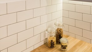 Een keuken met een witte betegelde achterwand, een houten aanrechtblad, een hanglamp en potten met pasta.