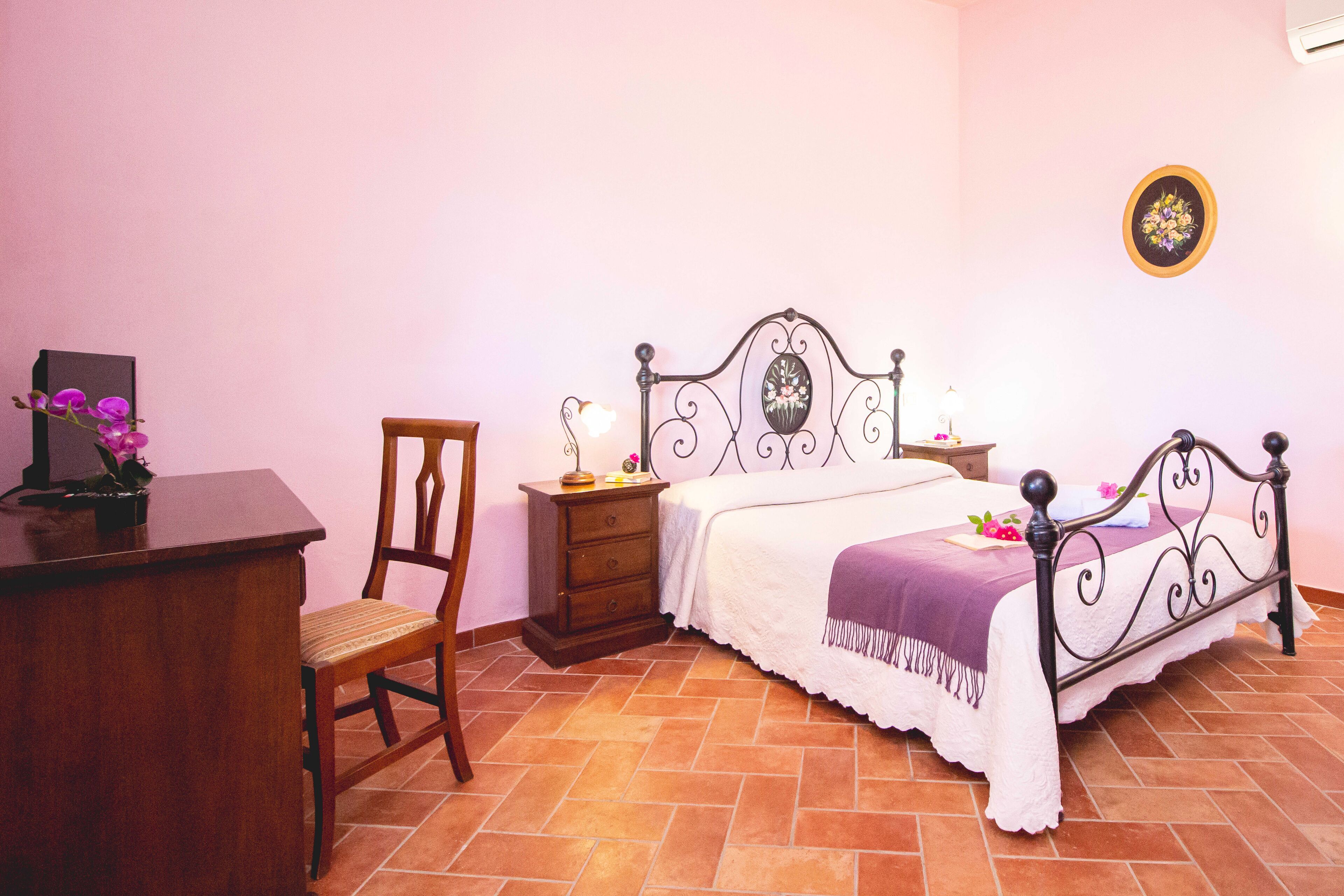 A bedroom with a bed, a wooden desk, a chair, a nightstand, and a wall-mounted picture.