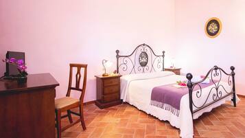 A bedroom with a bed, a wooden desk, a chair, a nightstand, and a wall-mounted picture.
