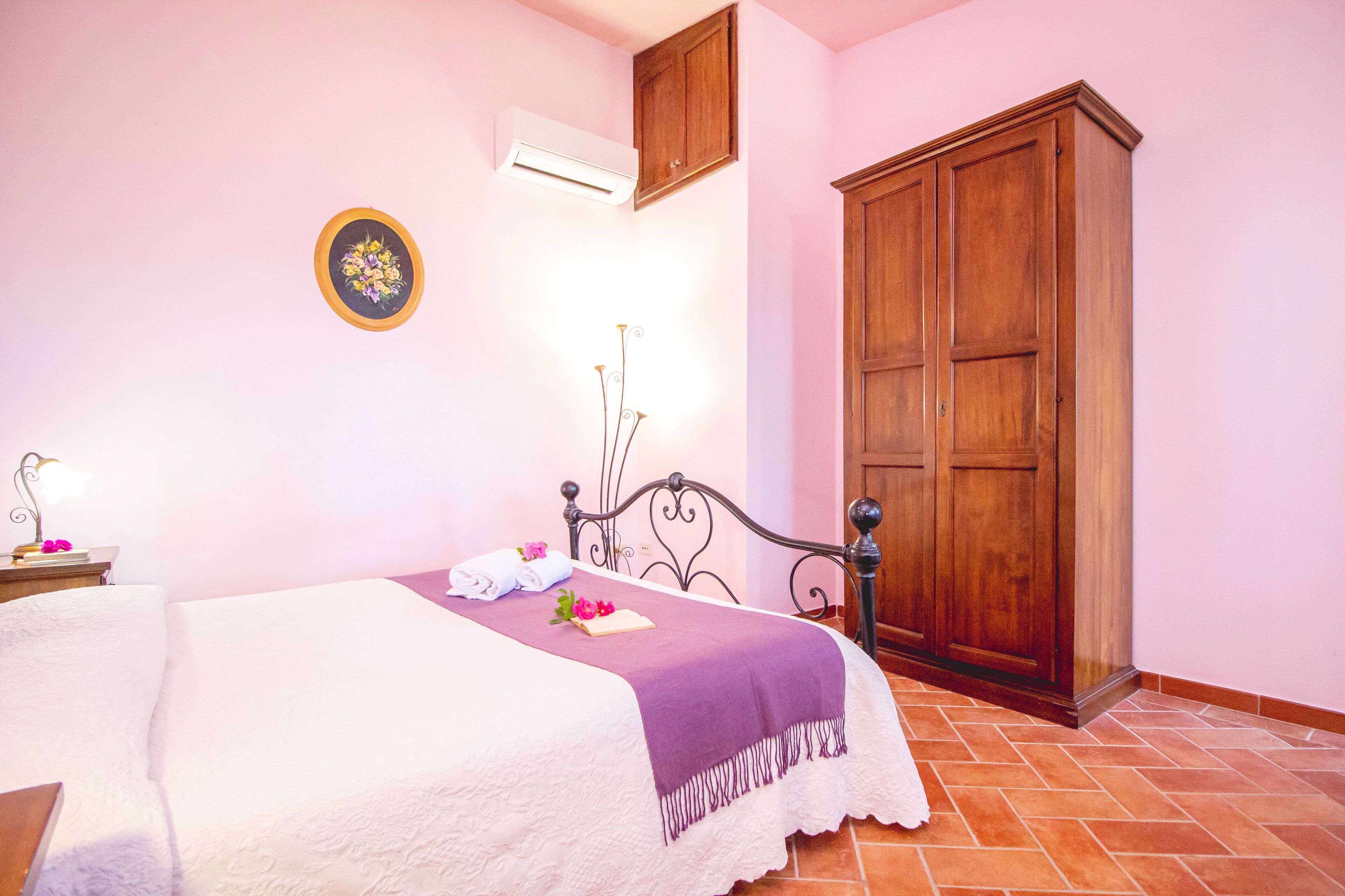 Un letto rifatto con una coperta bianca e viola, un armadio in legno e un condizionatore d'aria a parete.