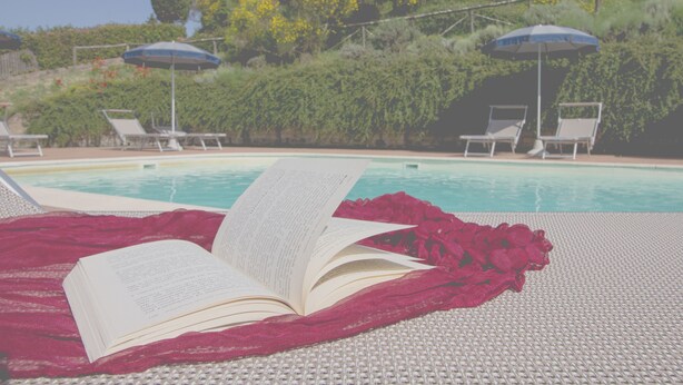 Ein Poolbereich mit Liegestühlen und Sonnenschirmen, ein Buch auf einem Handtuch und ein Pool im Hintergrund.