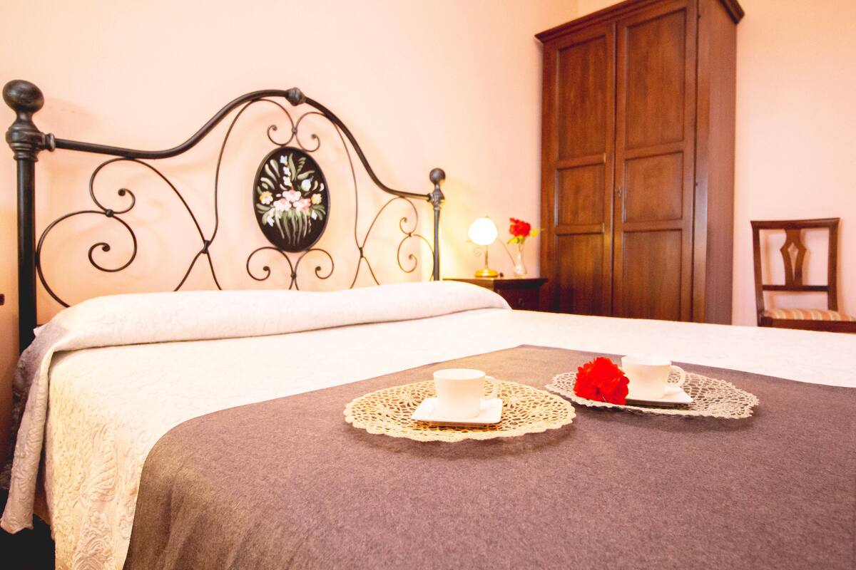 Un lit bien fait, agrémenté d’une tête de lit décorative, une table de chevet avec une lampe et une armoire en bois.