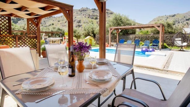 An outdoor dining area with a table set for two, overlooking a pool and hills. - Stergios Villa (Rhodes)