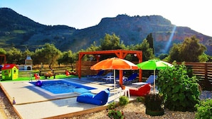 A pool area with lounge chairs, umbrellas, and a small playhouse. - Stergios Villa (Rhodes)
