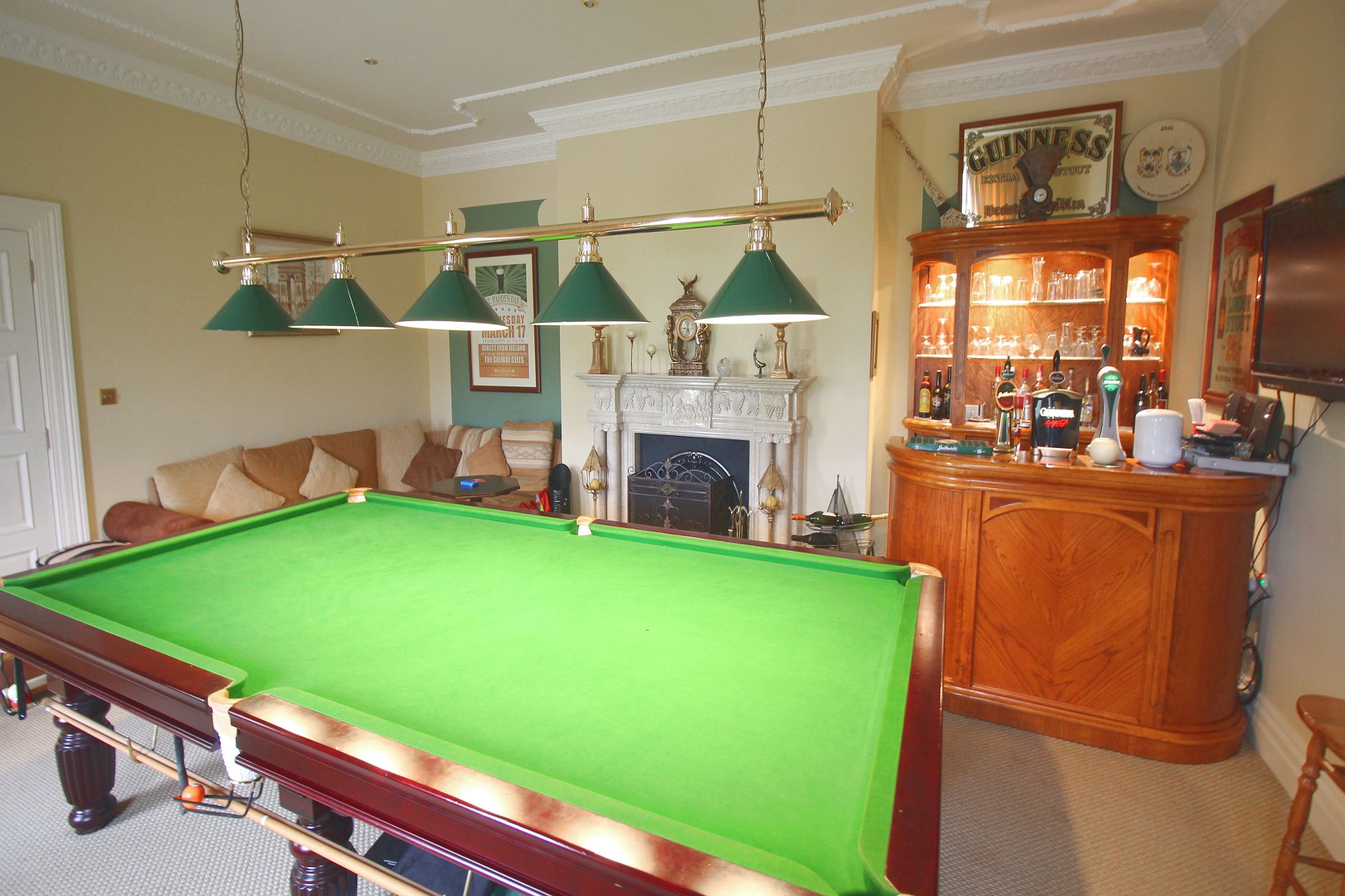 A pool table with a green felt surface, a wooden cabinet with glassware, and a fireplace with a mantel.