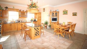 Een ruime keuken met houten kastjes, een centraal kookeiland met barstoelen, een eettafel met stoelen en een aan de muur bevestigde televisie.