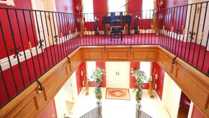 Een statige kamer, uitgevoerd in rood en wit, met een piano en een kroonluchter.