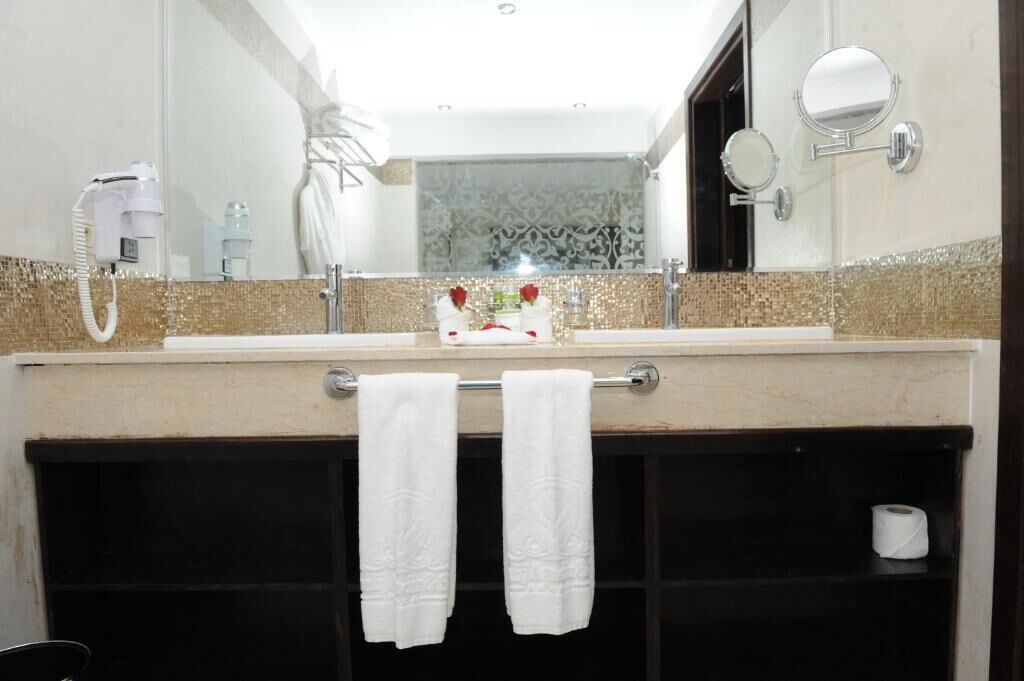 Un bagno con un ampio specchio, un portasciugamani con due asciugamani, un lavandino e un porta carta igienica.
