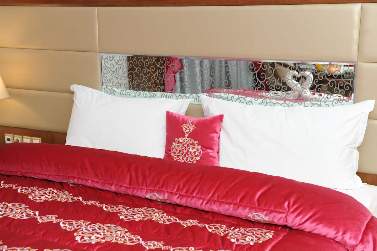 Une chambre d’hôtel avec un lit, des oreillers blancs et rouges, et un miroir décoratif au-dessus du lit.