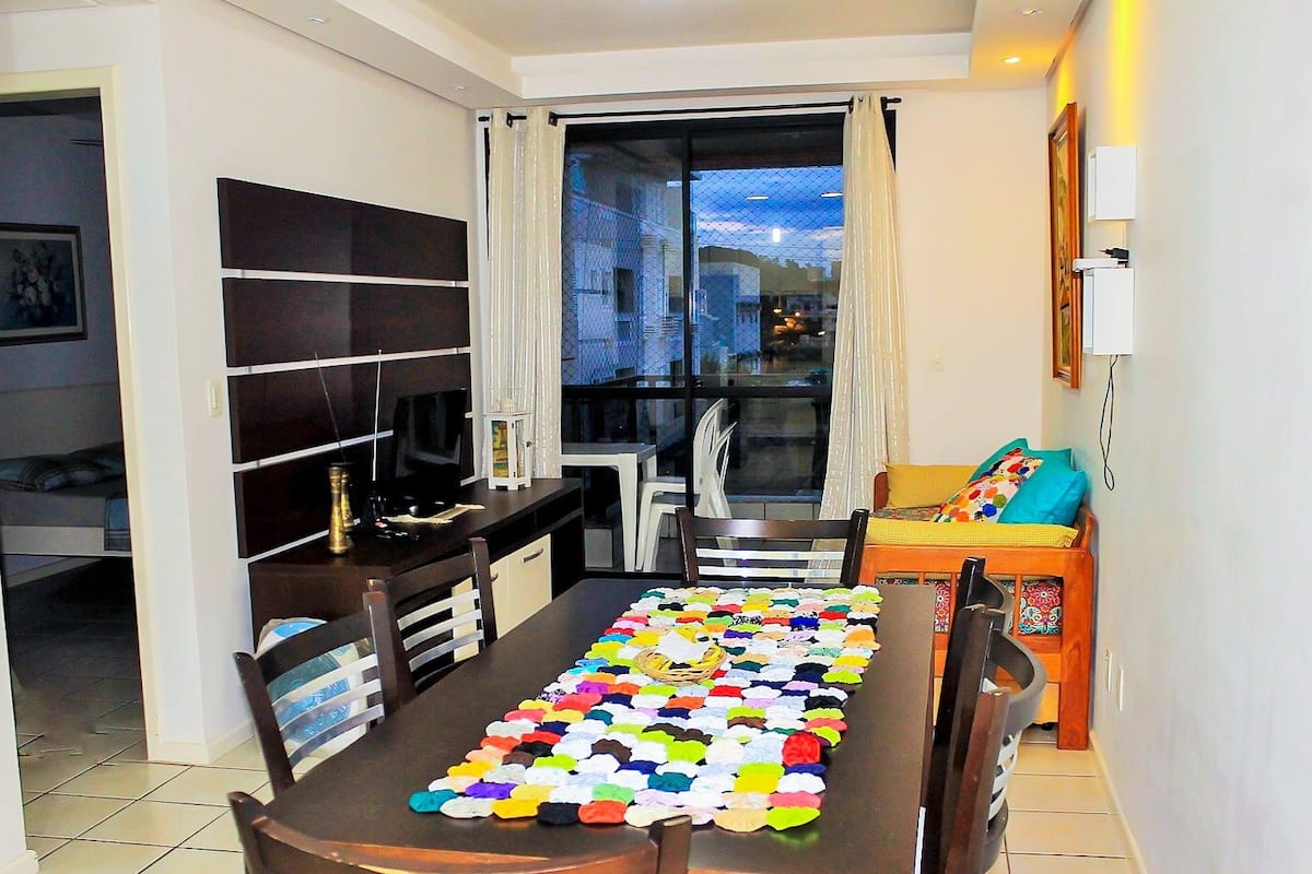 A compact living space with a dining table covered with a colorful table runner, a television on a stand, and a small seating area with a sofa and chairs.
