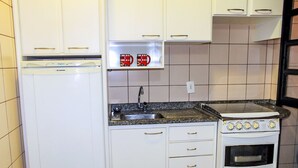A compact kitchen with white cabinets, a built-in oven, and a granite countertop. - Apartamento Leonardi (Florianópolis)