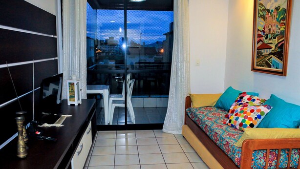 A small, modern living room with a sofa, a dining table, and a kitchen area. - Apartamento Leonardi (Florianópolis)