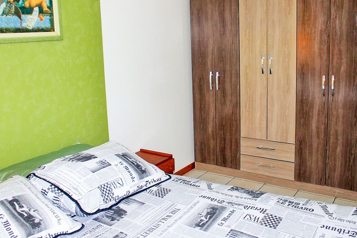 A bedroom with a bed covered in newspapers, a green wall, and a wooden wardrobe with two doors.