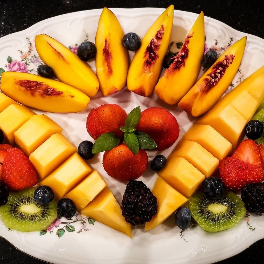 Una bandeja de frutas con melocotones, fresas, arándanos, zarzamoras y kiwi sobre un plato con estampado floral.