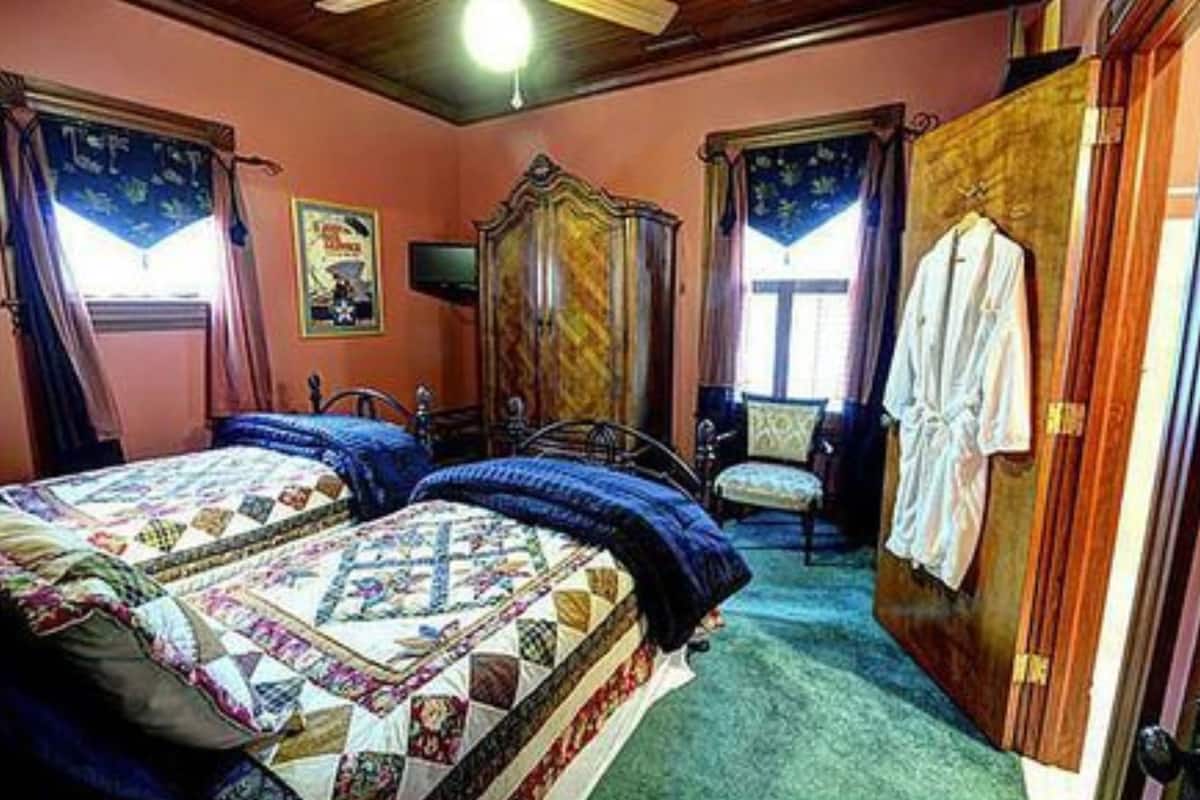 Un dormitorio con dos camas, un armario de madera, una silla y un ventanal con cortinas.