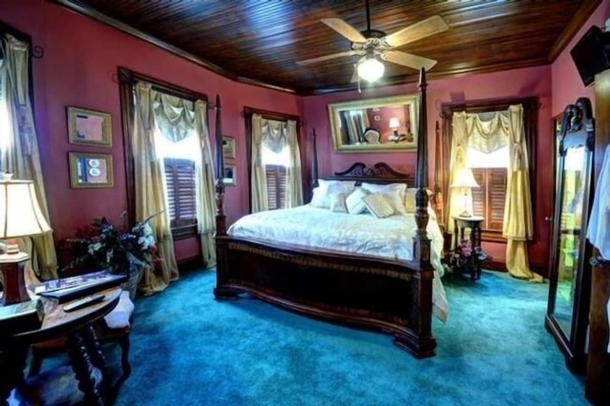 Un dormitorio con una cama de madera, un ventilador de techo y una alfombra azul.