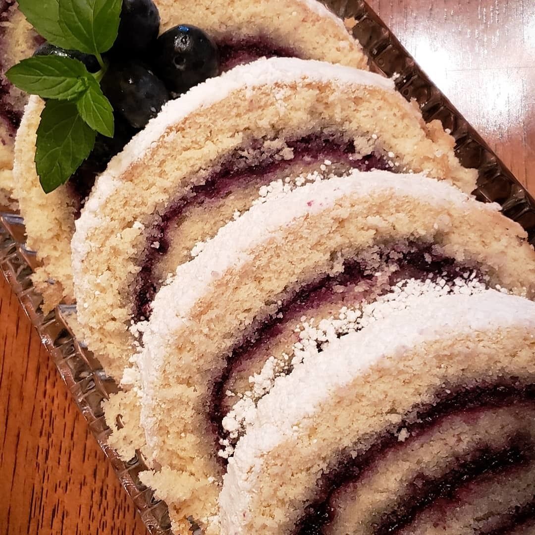 Un postre enrollado con una capa exterior desmenuzable, posiblemente un pastel o un hojaldre, sobre un plato de vidrio.