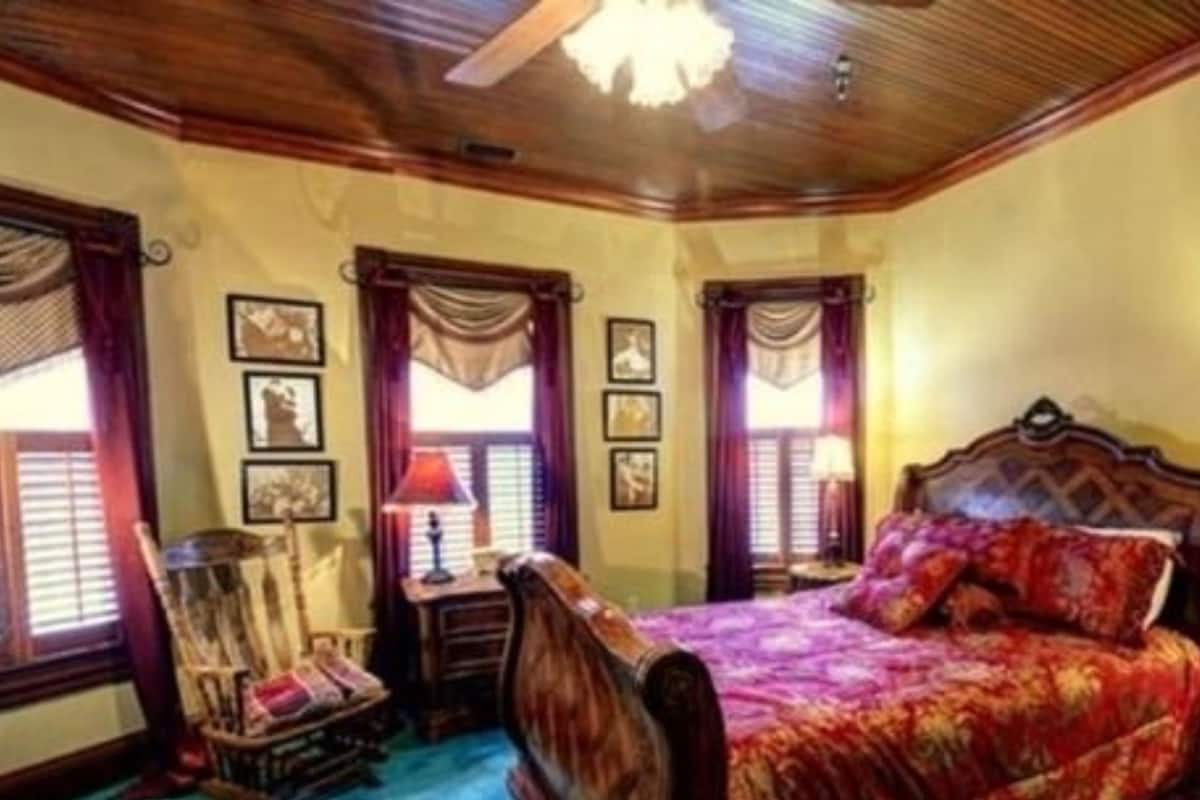 Un dormitorio con techo de madera, una cama grande con colcha estampada, una mesita de noche con lámpara y una silla.