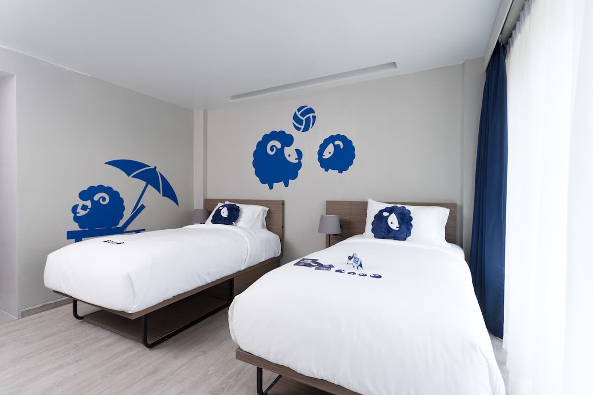 Habitación de hotel con dos camas, un mural en la pared y una ventana con cortinas.