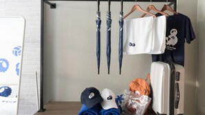Et pænt og ryddeligt værelse med et træskrivebord, en knagerække med paraplyer og en t-shirt, en kuffert og pænt foldede sko.