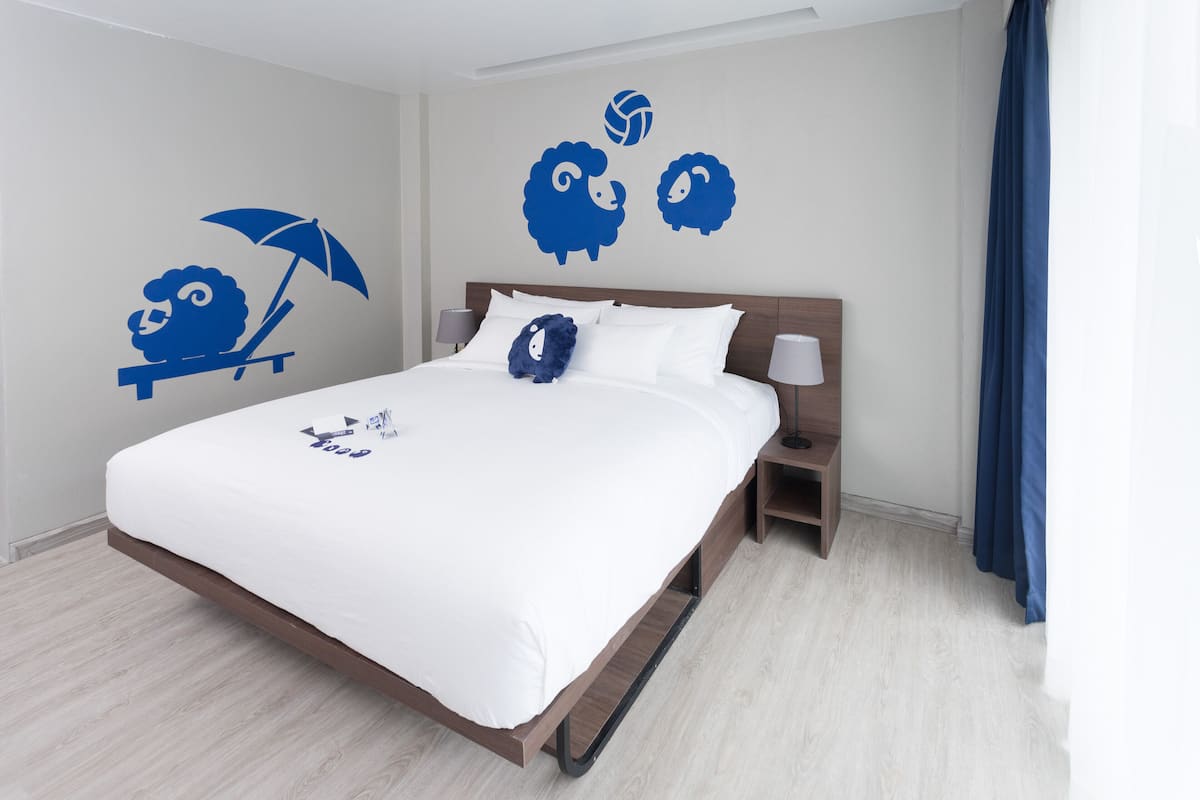 Una cama bien hecha con sábanas blancas, cabecera de madera y mesita de noche con lámpara.
