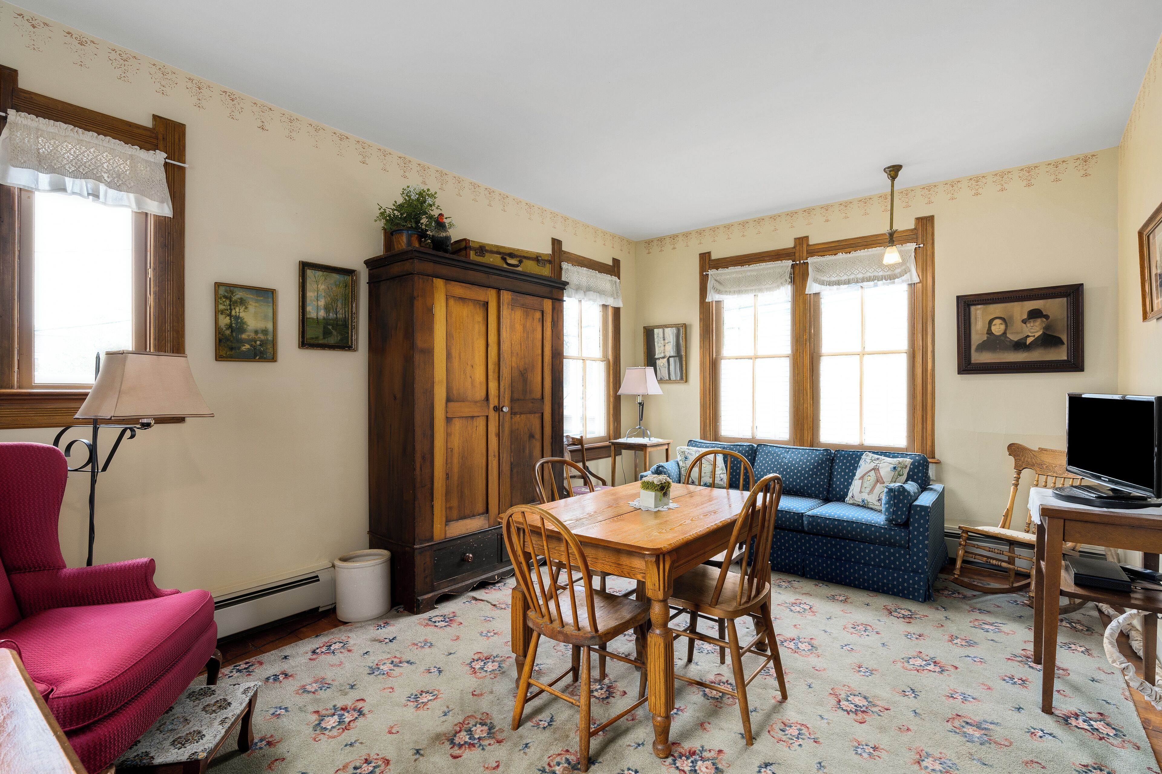 A cozy living room with a wooden dining table, blue sofa, and a red armchair.