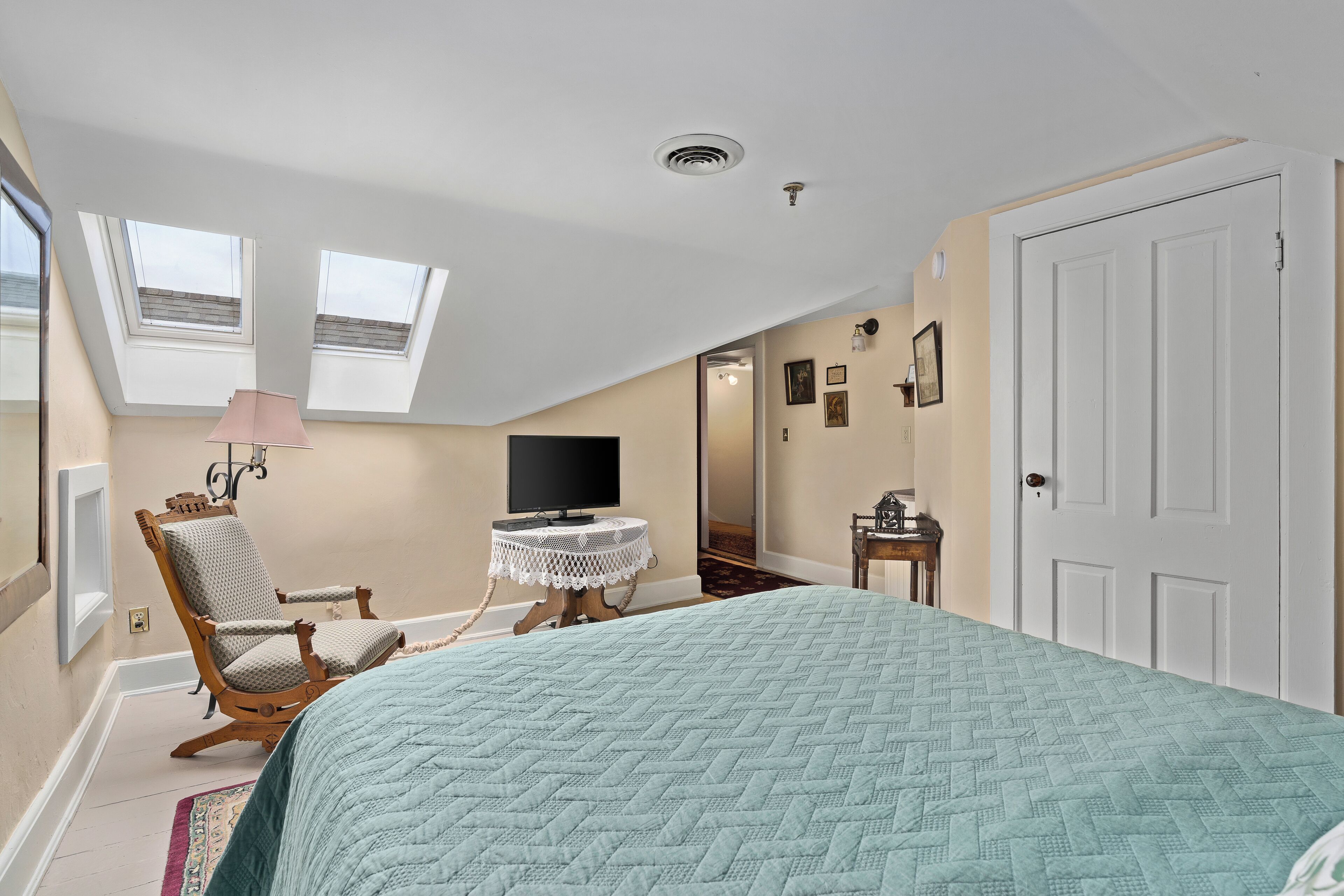 A bedroom with a bed, a chair, a small table, a TV, and a ceiling fan.