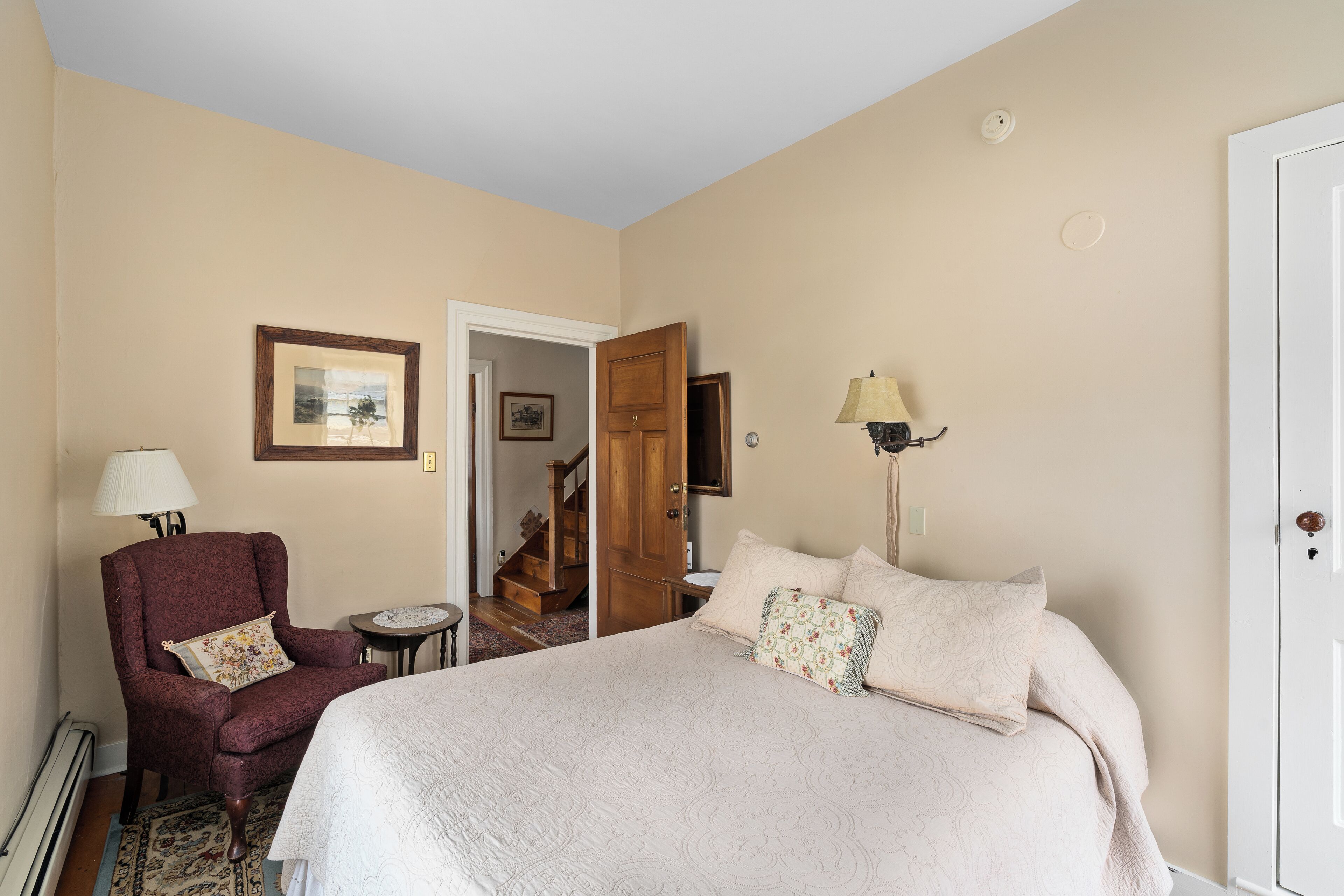 A hotel room with a large bed, a chair, a lamp, and a door leading to a staircase.