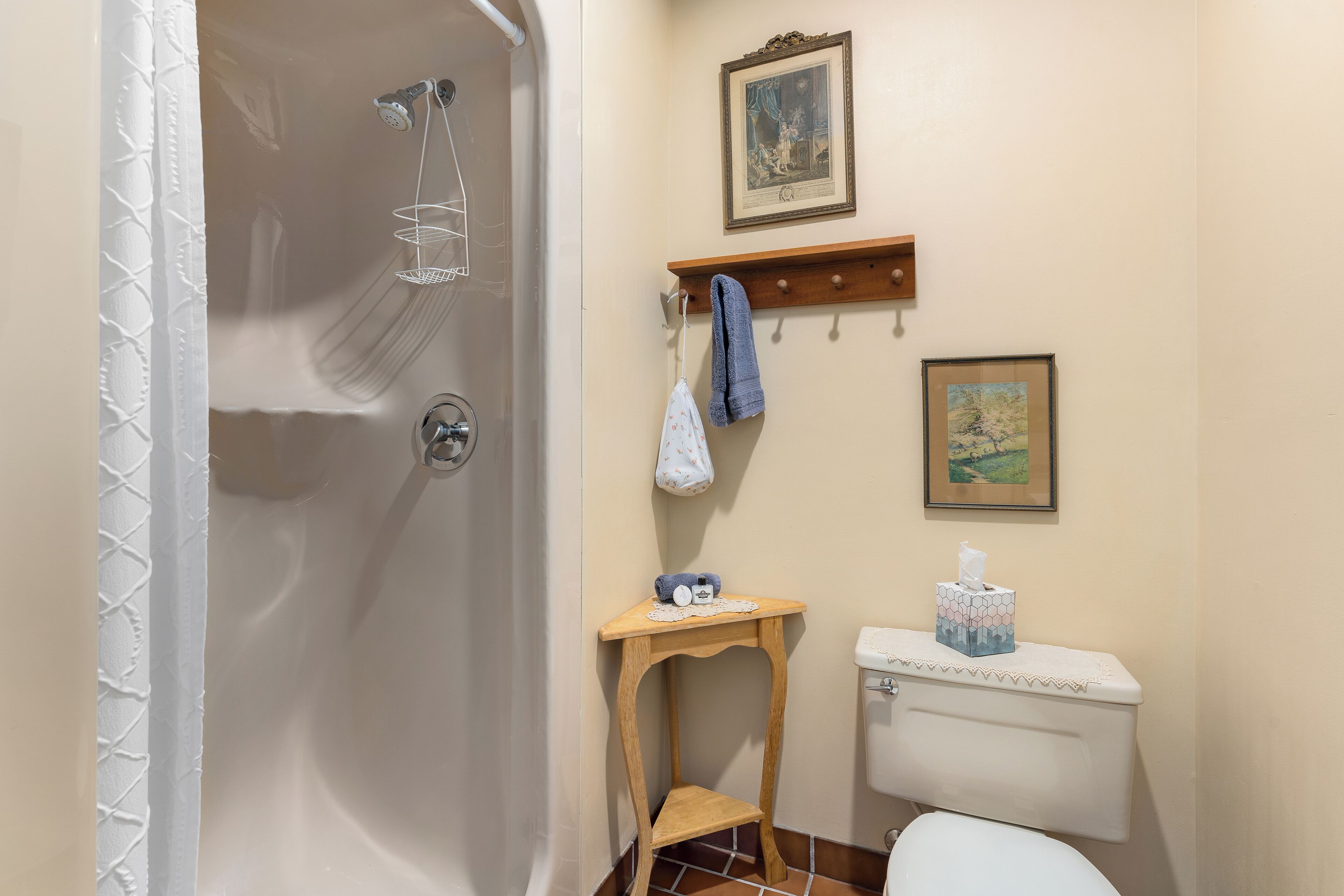 A bathroom with a shower, toilet, and a small wooden table with a towel and a tissue box.