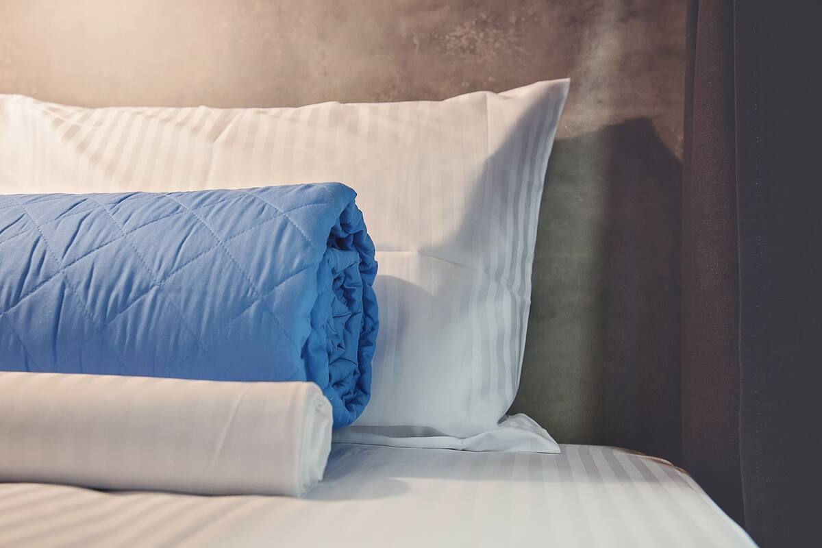 Ein ordentlich bezogenes Bett mit einer blauen Bettdecke und weißen Kissen.