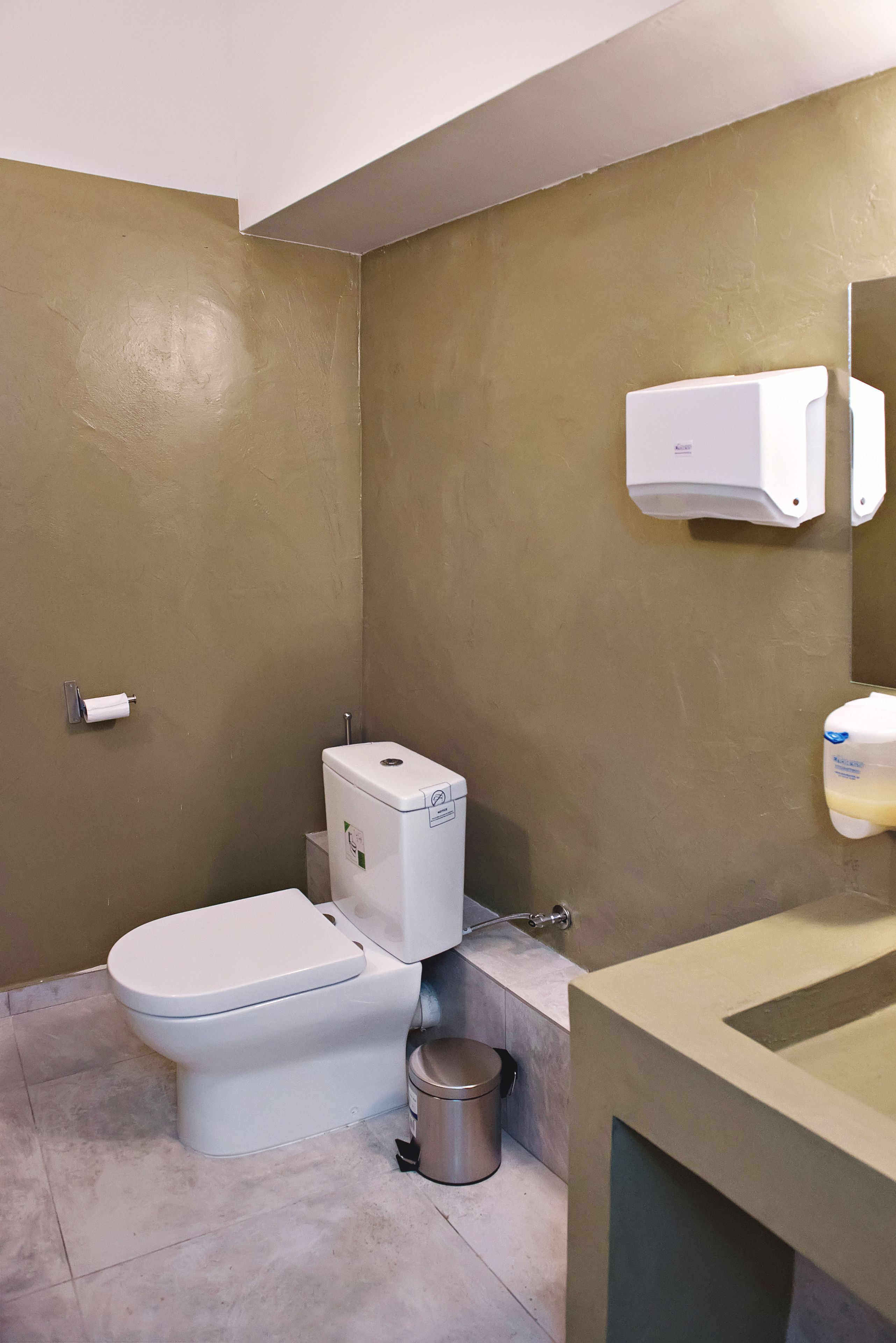 A small bathroom with a toilet, a trash can, and a hand dryer.