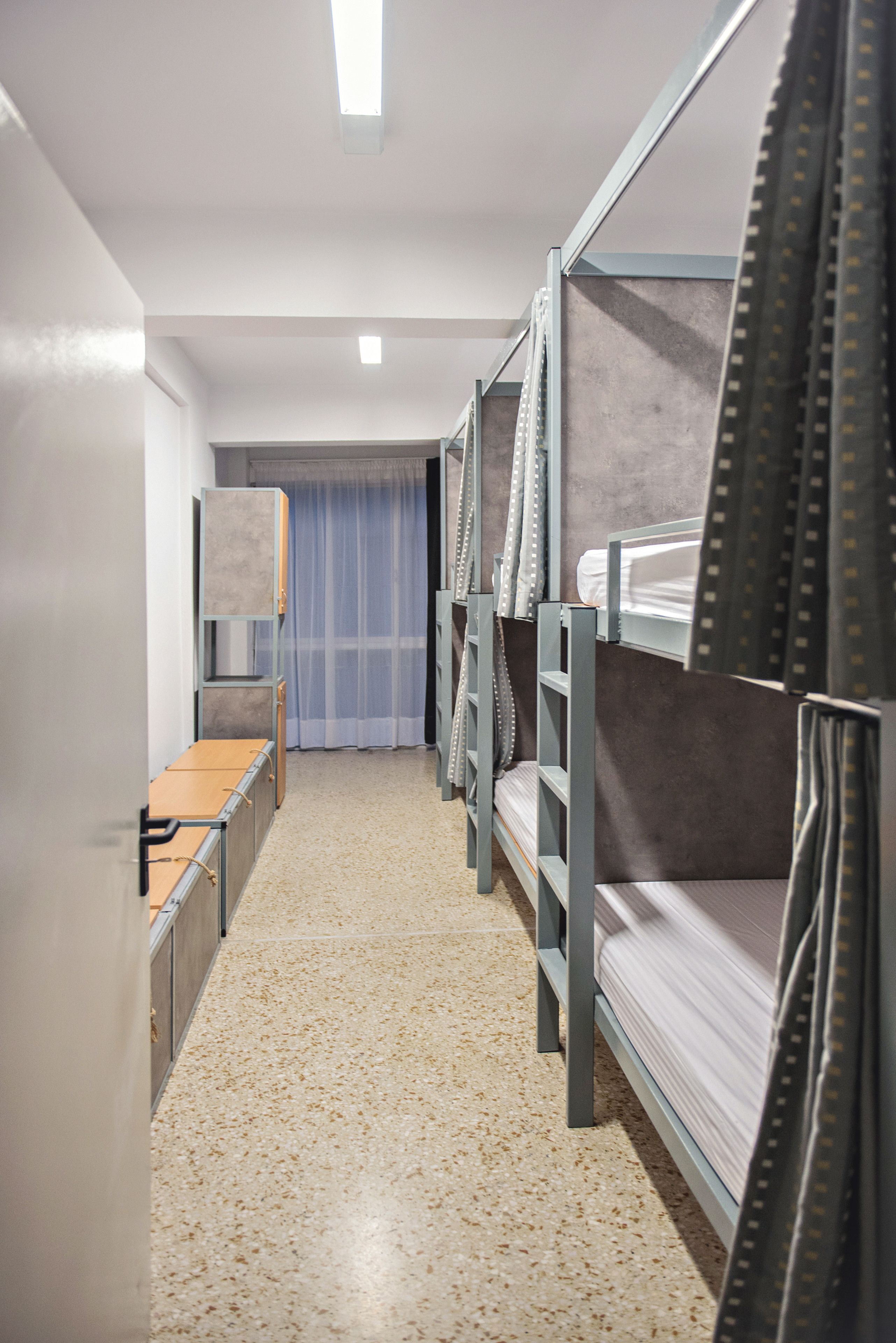 A narrow corridor with bunk beds, a small desk, and a window with curtains.