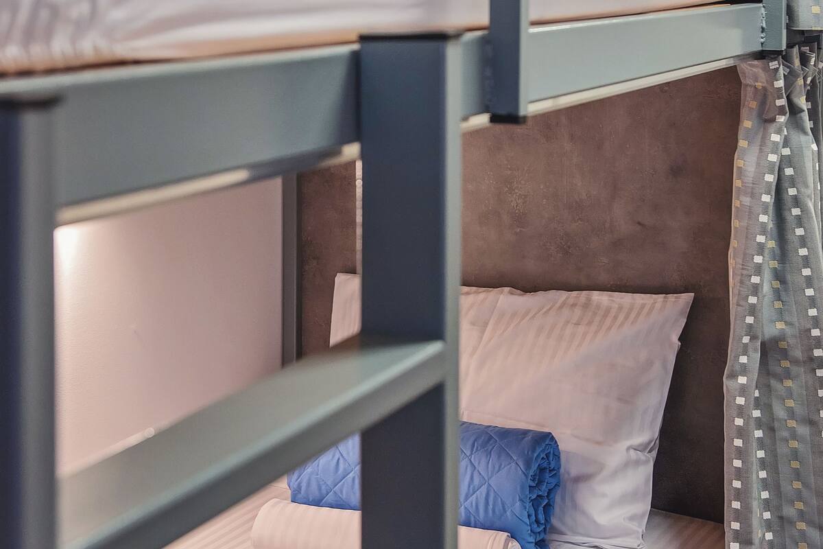 Ein Stockbett mit grauem Metallgestell, weißer Bettwäsche und einem blau gesteppten Kissen.