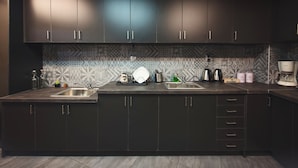 A modern kitchen with dark cabinets, a patterned backsplash, and a central island with a sink. - Bedbox Hostel (Athens)