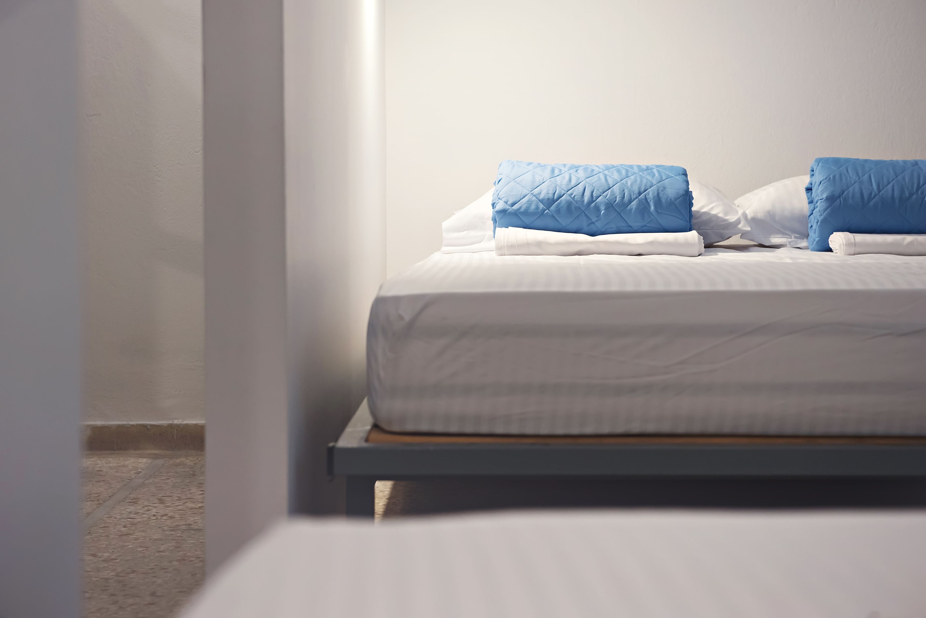 A neatly made bed with white and blue bedding, a wooden headboard, and a plain white wall.