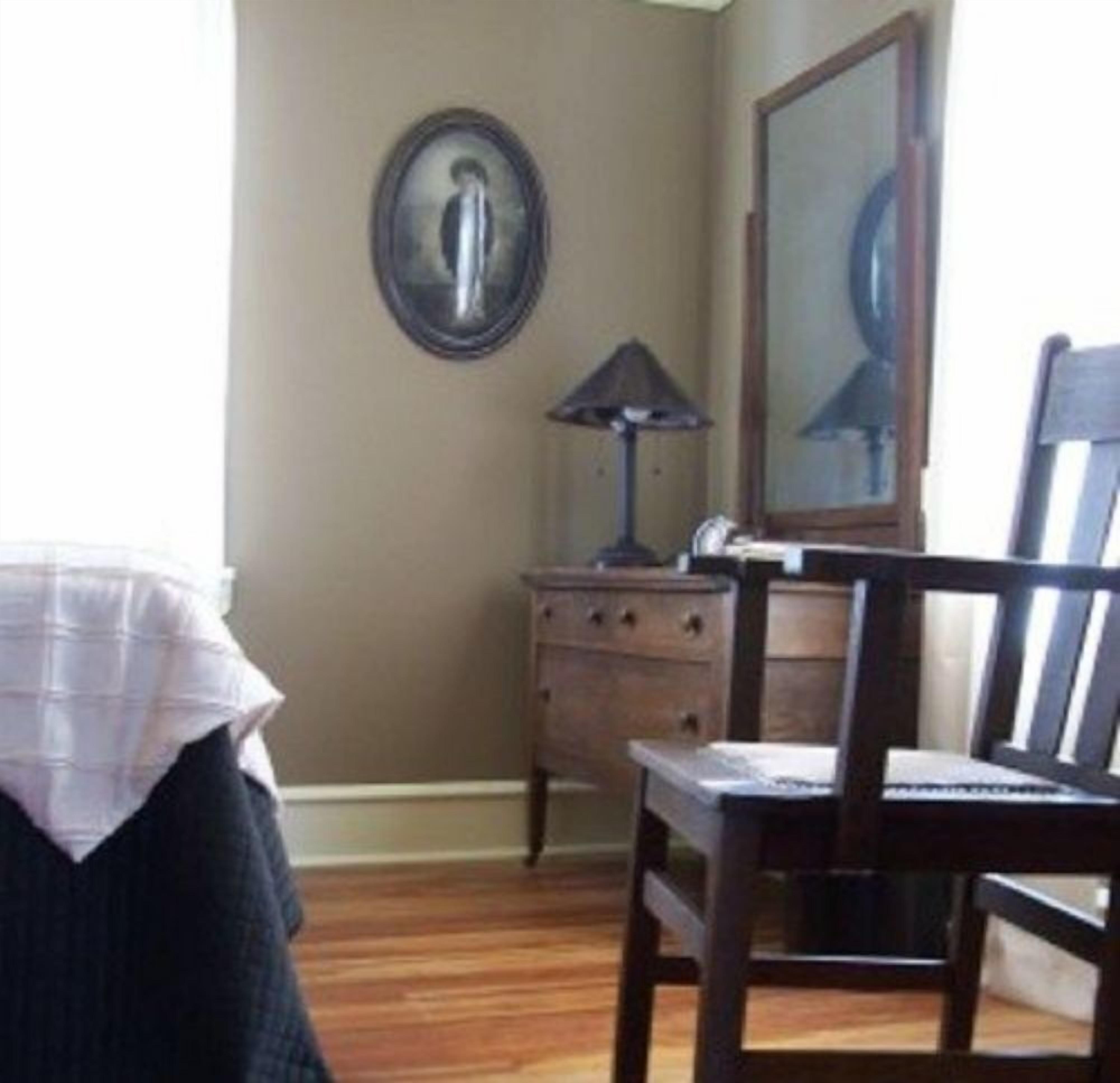 A room with a bed, a wooden dresser, a chair, and a mirror on the wall.