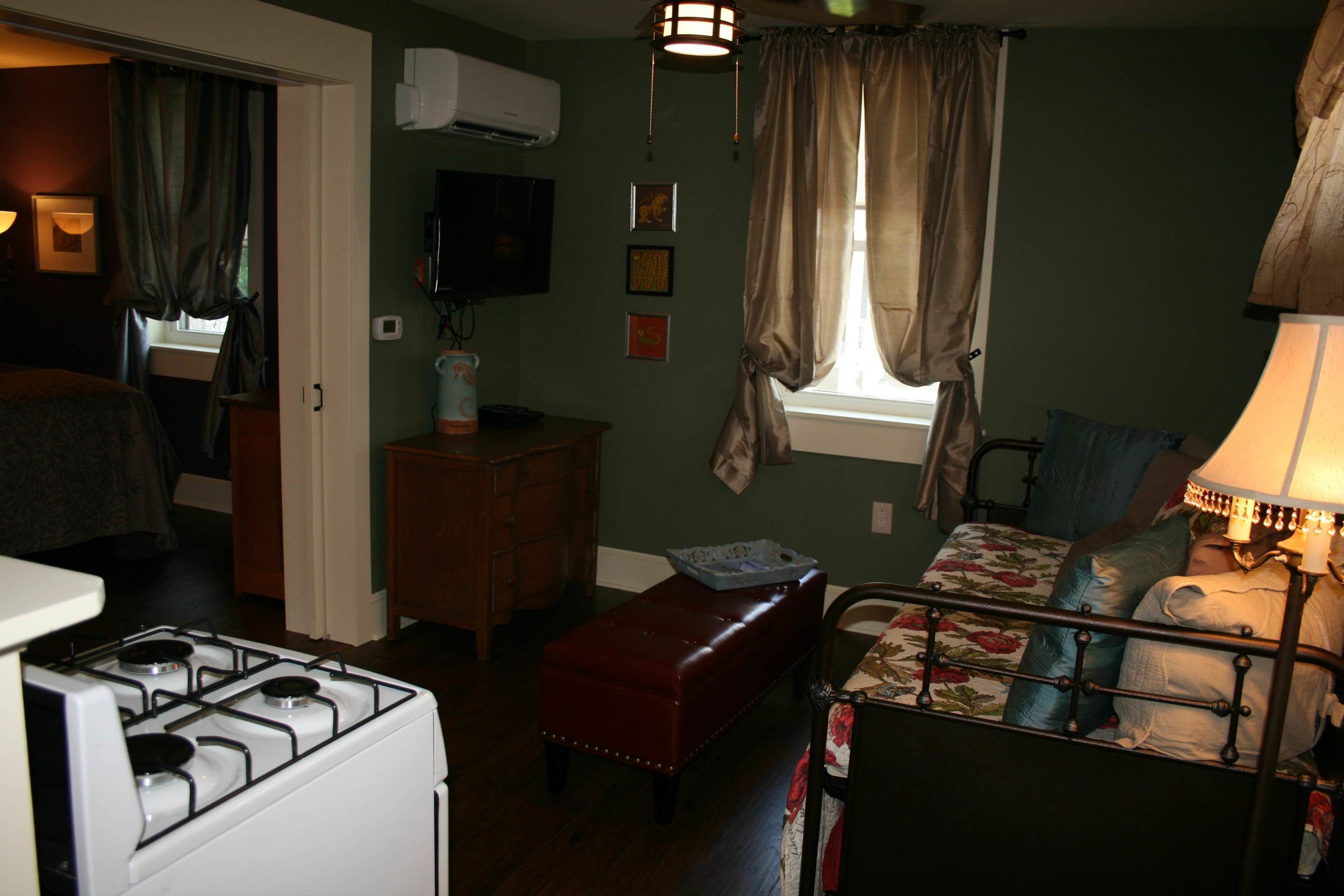 A compact bedroom with a bed, a small table, a red bench, and a stove.