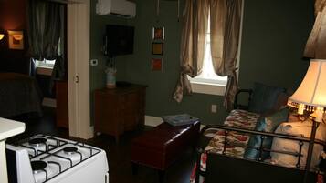 A compact bedroom with a bed, a small table, a red bench, and a stove.