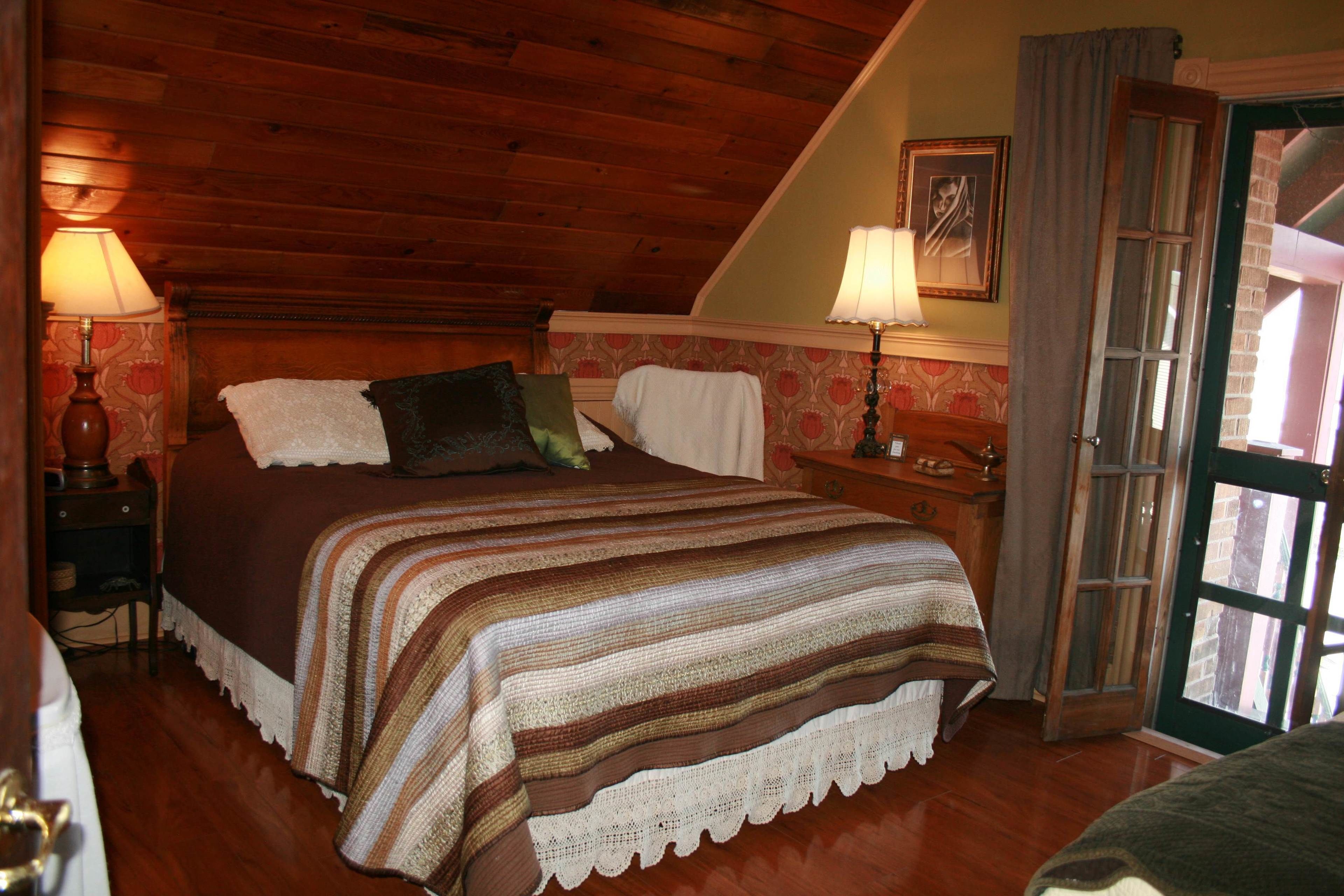 Una camera da letto accogliente con soffitto in legno, un letto grande con coperta a righe, due lampade da comodino e una finestra con tende.