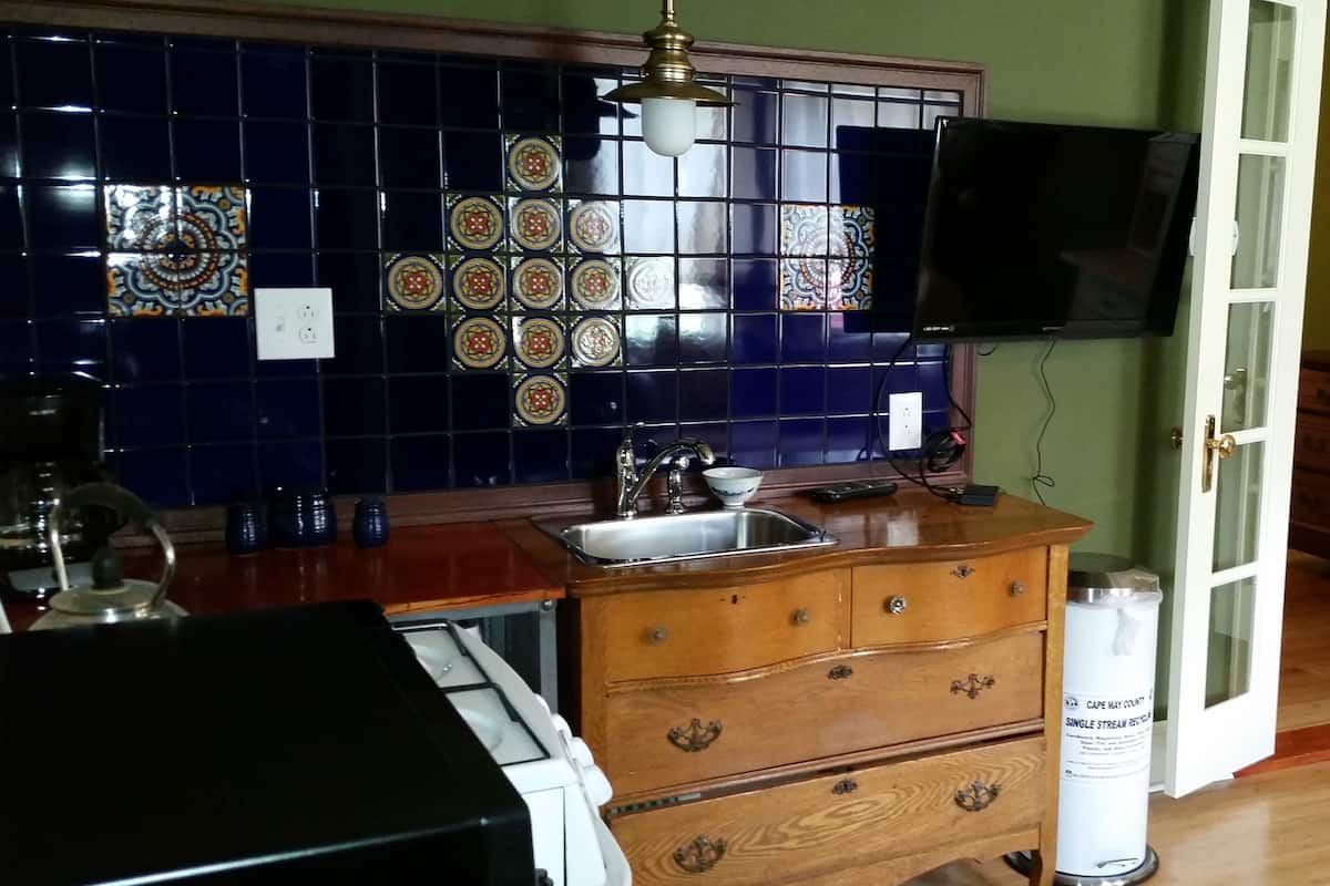 A kitchen with a wooden countertop, a sink, and a stove. There is a decorative backsplash with blue tiles and a television mounted on the wall.