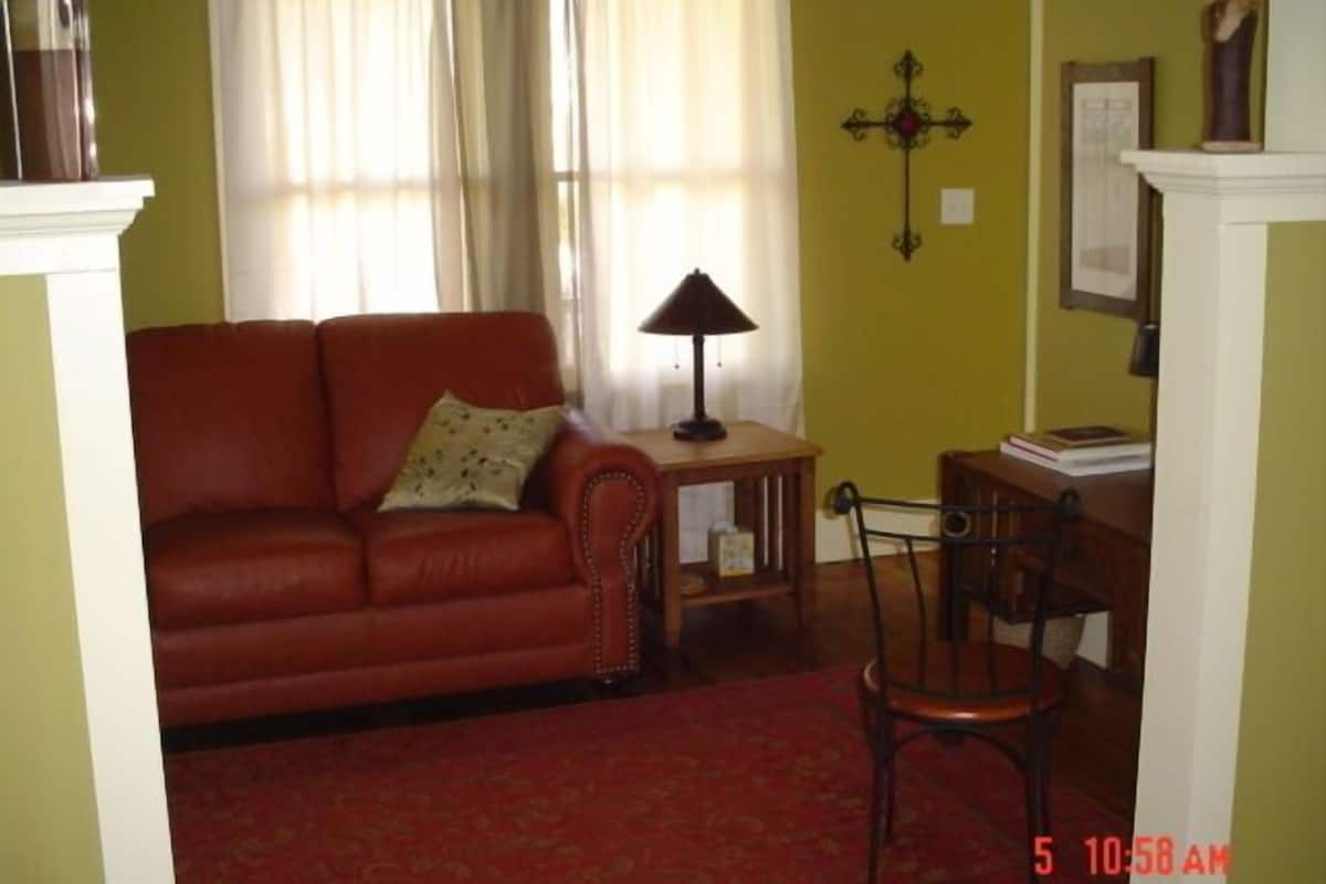 A living room with a red sofa, a small table with a lamp, a wooden chair, and a red carpet.