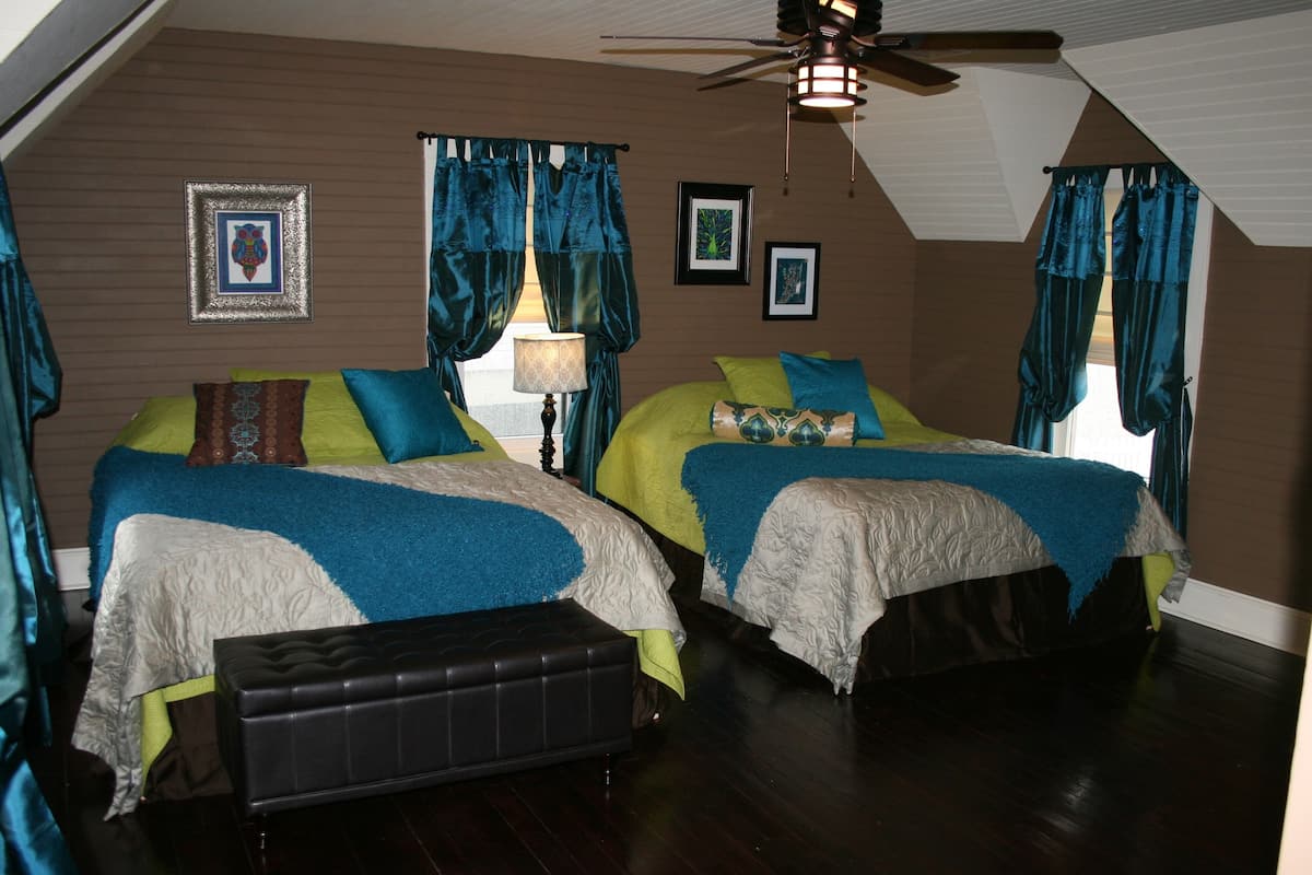 A room with two beds, a ceiling fan, and a wooden floor.