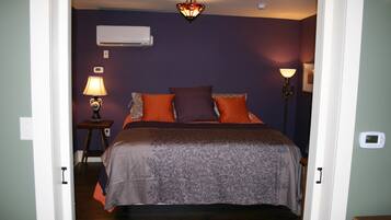 A bedroom with a bed, an air conditioner, a lamp, and a thermostat.