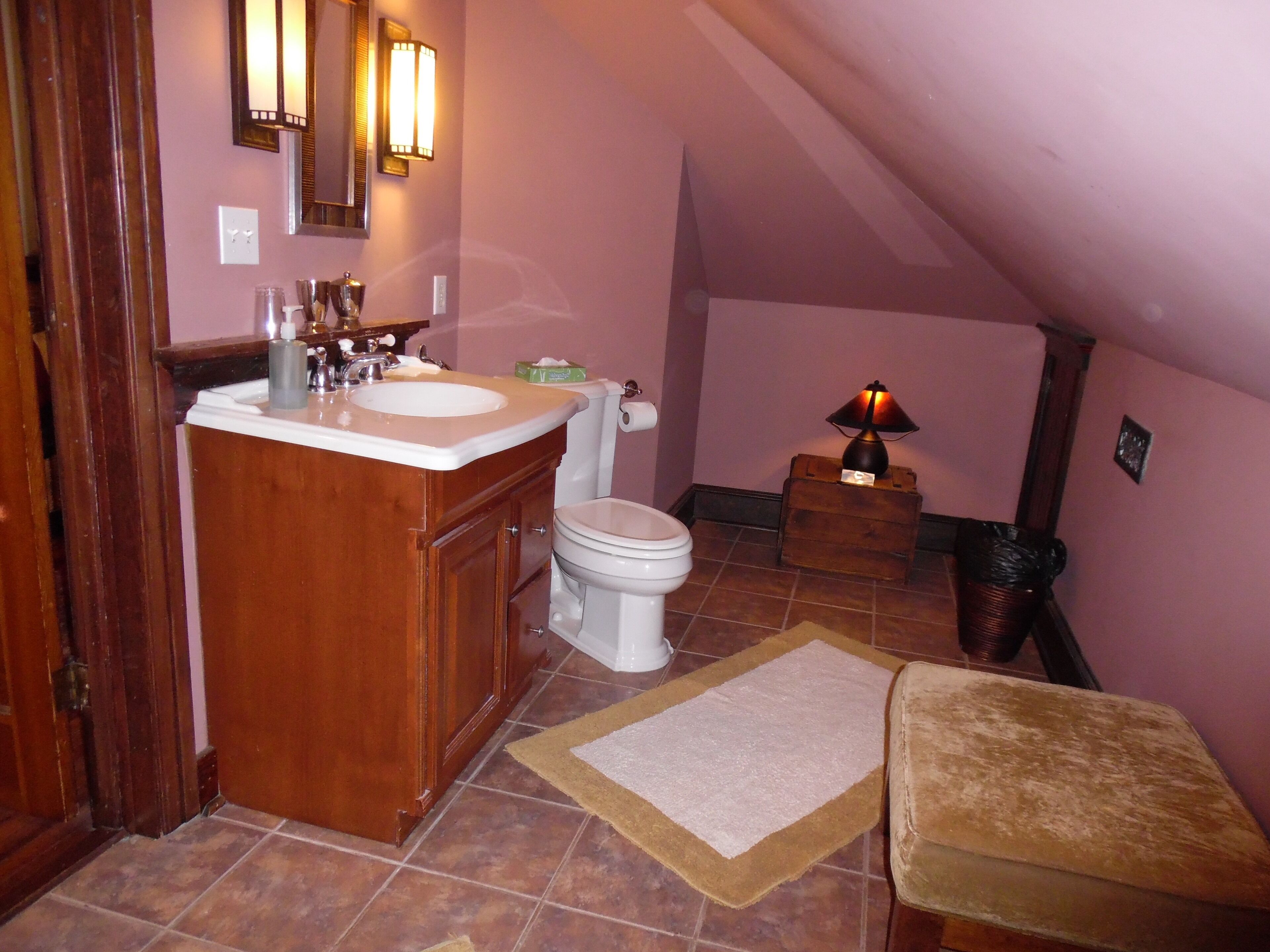 A small bathroom with a wooden vanity, a toilet, a sink, and a lamp.