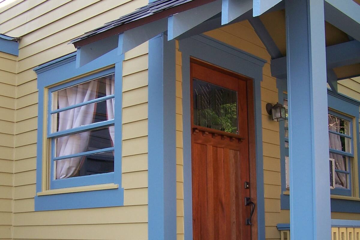 A house with a wooden front door, a window with curtains, and a blue exterior.