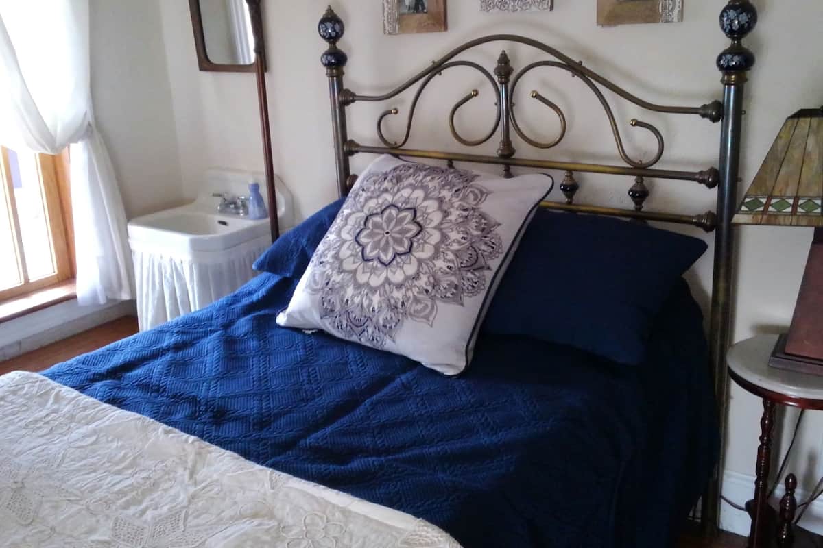 A bed with a blue quilt and a decorative pillow, a bedside table, a lamp, and framed pictures on the wall.