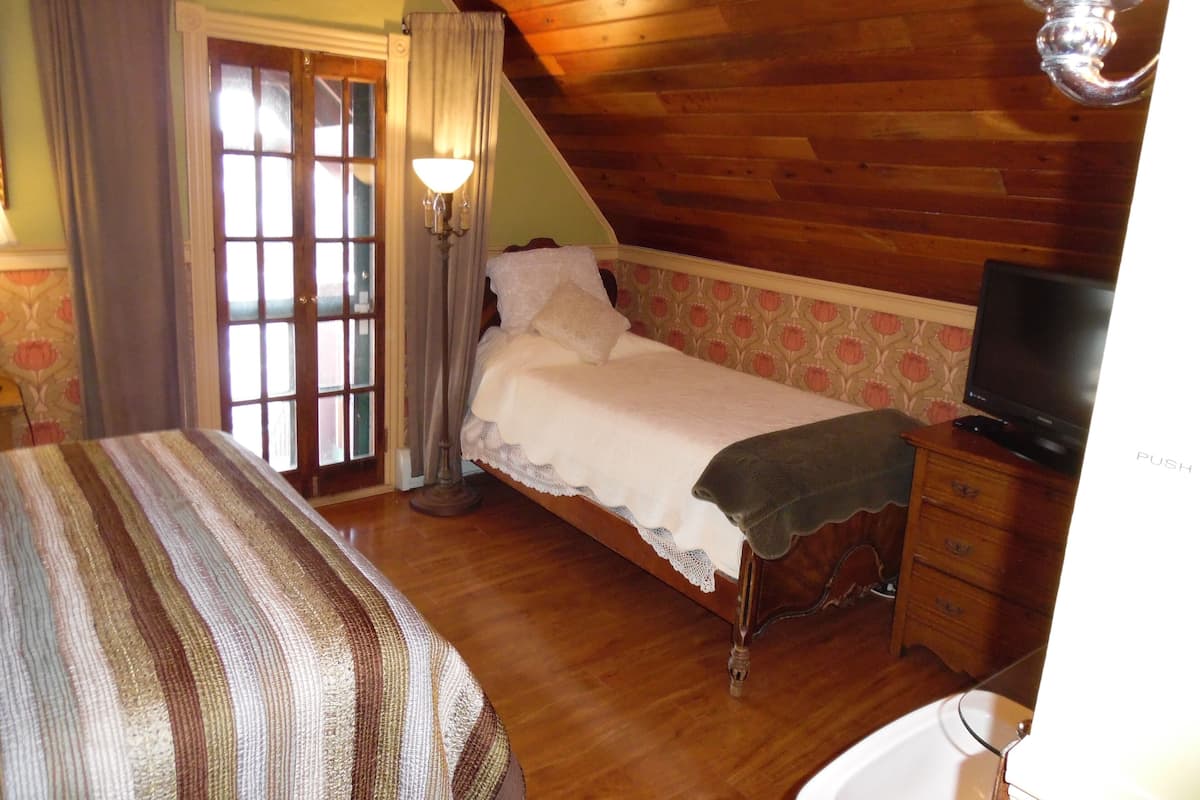 A bedroom with a bed, a television, a dresser, and a window with curtains.