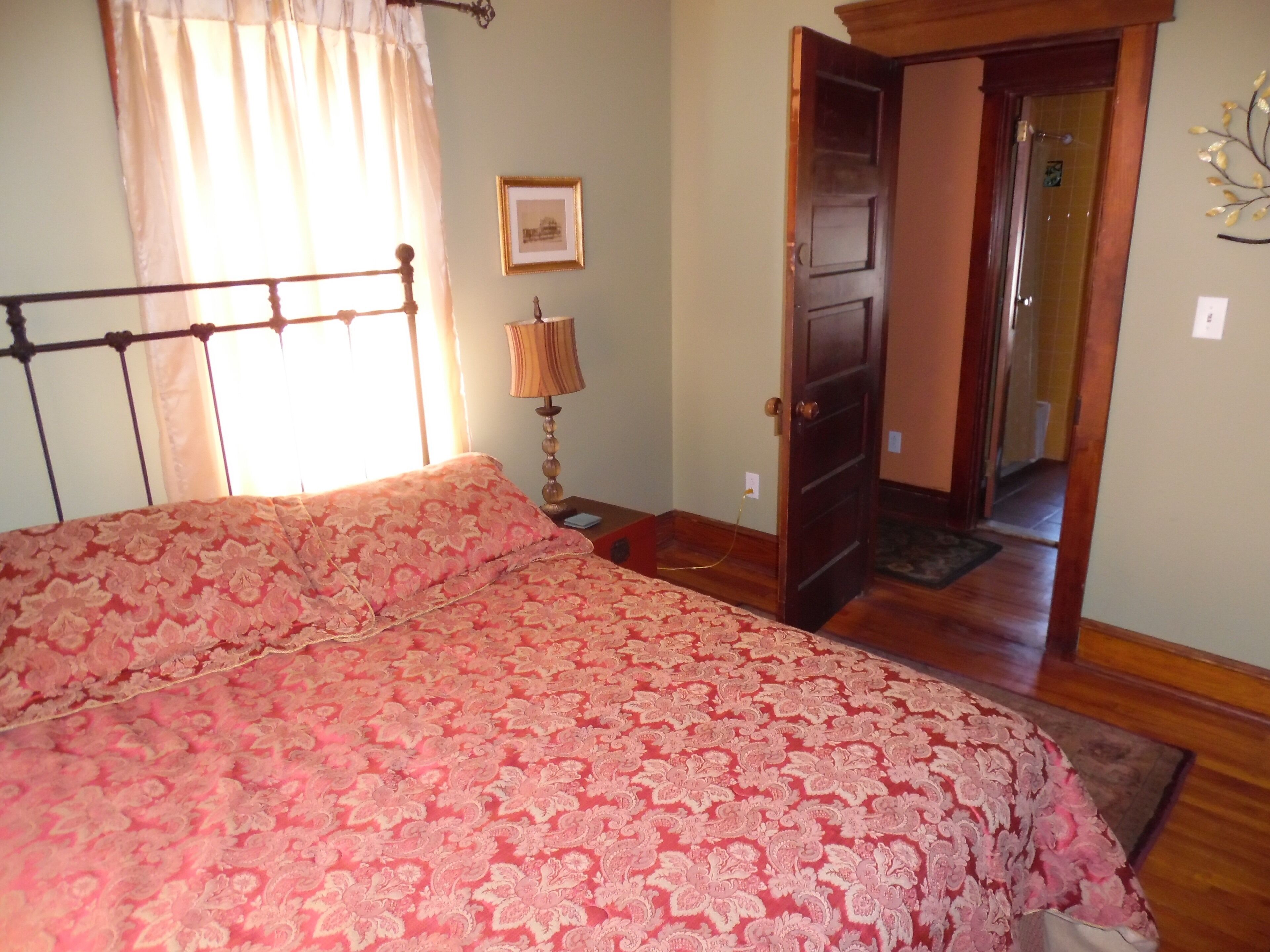 Une chambre à coucher avec un lit, une table de chevet, une lampe, une porte et un tableau accroché au mur.